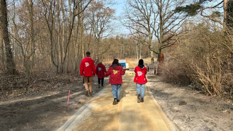 Vier Personen in roten LAGA-Jacken gehen über einen neu gepflasterten Weg auf dem künftigen Gartenschau-Gelände