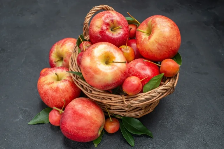 Frisch geerntete rote Äpfel und kleine Zieräpfel mit Blättern in einem Weidenkorb